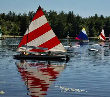 A small sailboat with a red striped sail being operated by a camper at this sleep away summer camp for boys in Pennsylvania.
