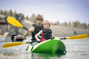 Children kayaking together in a green kayak at summer camp outdoor adventure